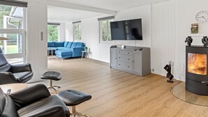 Een moderne woonkamer met een blauwe modulaire bank, een flatscreen televisie, een grijze kast en een houtkachel.