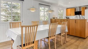 Een moderne keuken met houten kastjes, een roestvrijstalen koelkast en een eethoek met een gestreepte tafelkleed en houten stoelen.