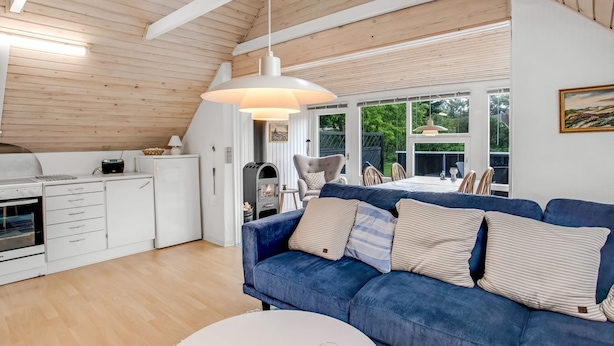 Una cocina moderna con horno empotrado, una zona de comedor con sofá azul y una mesa, y un amplio ventanal con vistas al exterior.