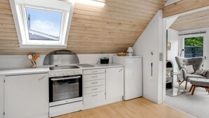 Una cocina moderna con armarios blancos, una estufa de acero inoxidable y un horno empotrado. Hay una ventana sobre el fregadero y una puerta que da a un balcón.