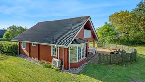 Une maison de plain-pied avec un toit en pente, une véranda et un jardin clôturé.