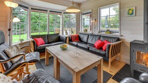 Un salon chaleureux avec une cheminée, des canapés en cuir, une table basse en bois et de grandes fenêtres donnant sur l’extérieur.