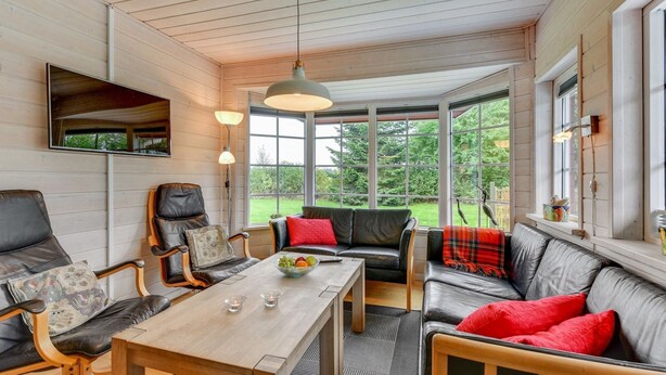Une pièce chaleureuse avec un plafond en bois, une table à manger, des canapés en cuir et une grande fenêtre donnant sur un paysage verdoyant.