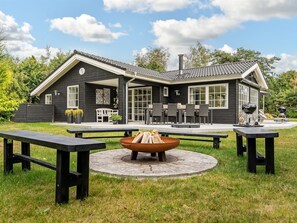 A two-story house with a patio area featuring a fire pit and picnic tables.