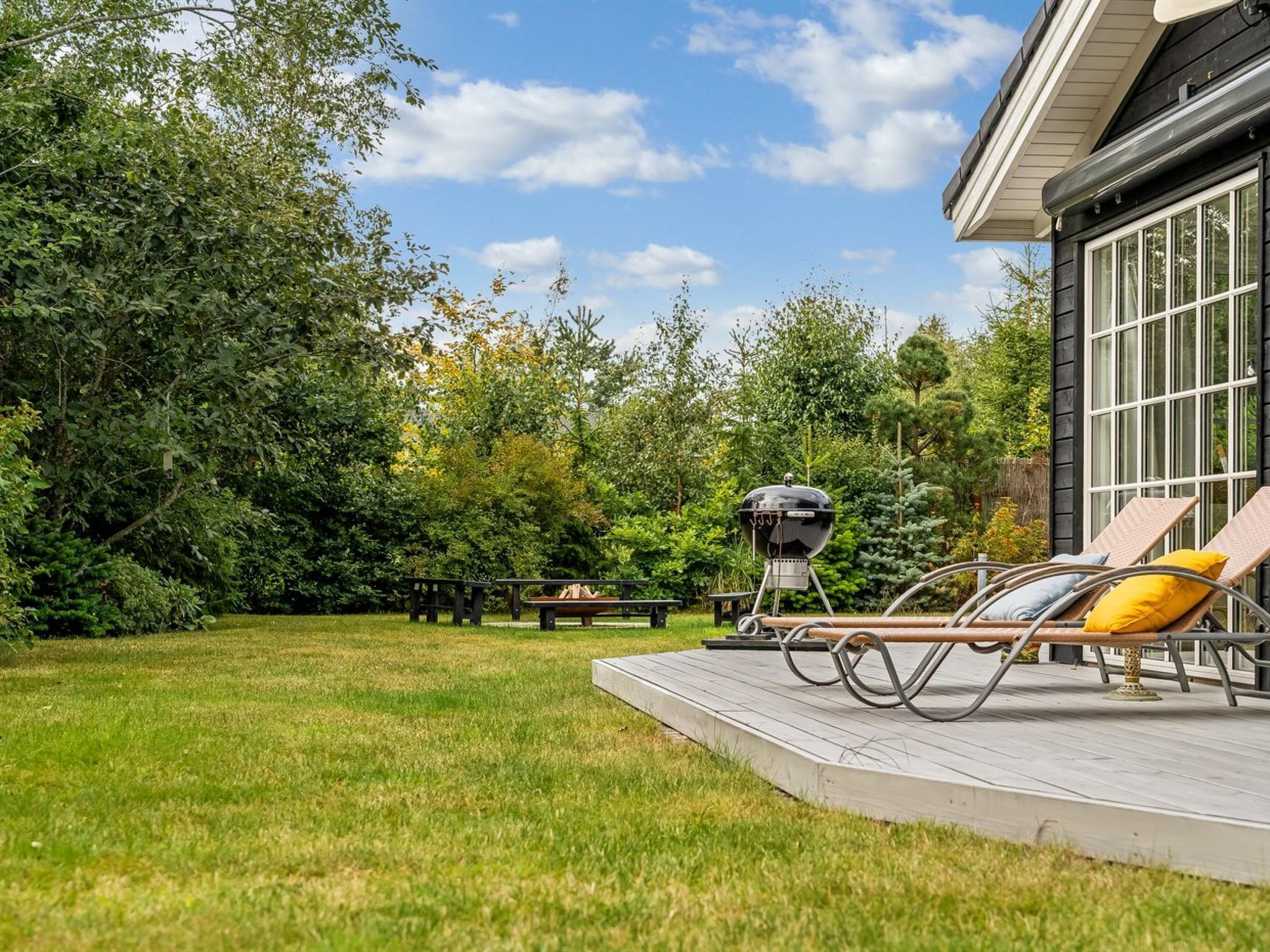 A deck with lounge chairs and a barbecue grill, surrounded by a grassy yard and trees.