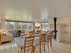 Uma sala de jantar acolhedora com uma mesa posta para quatro pessoas, rodeada por cadeiras de madeira, um sofá e uma lareira.