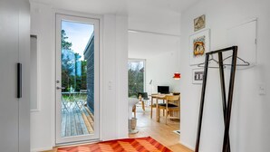 Un intérieur moderne avec un plancher en bois, un tapis à motifs chevrons, un coin repas comprenant une table et des chaises, et une vue sur une terrasse extérieure, accessible par une porte vitrée.