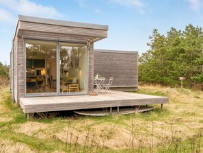 Una moderna baita con ingresso con porta in vetro, un pontile in legno e un'area pranzo con mobili da esterno.
