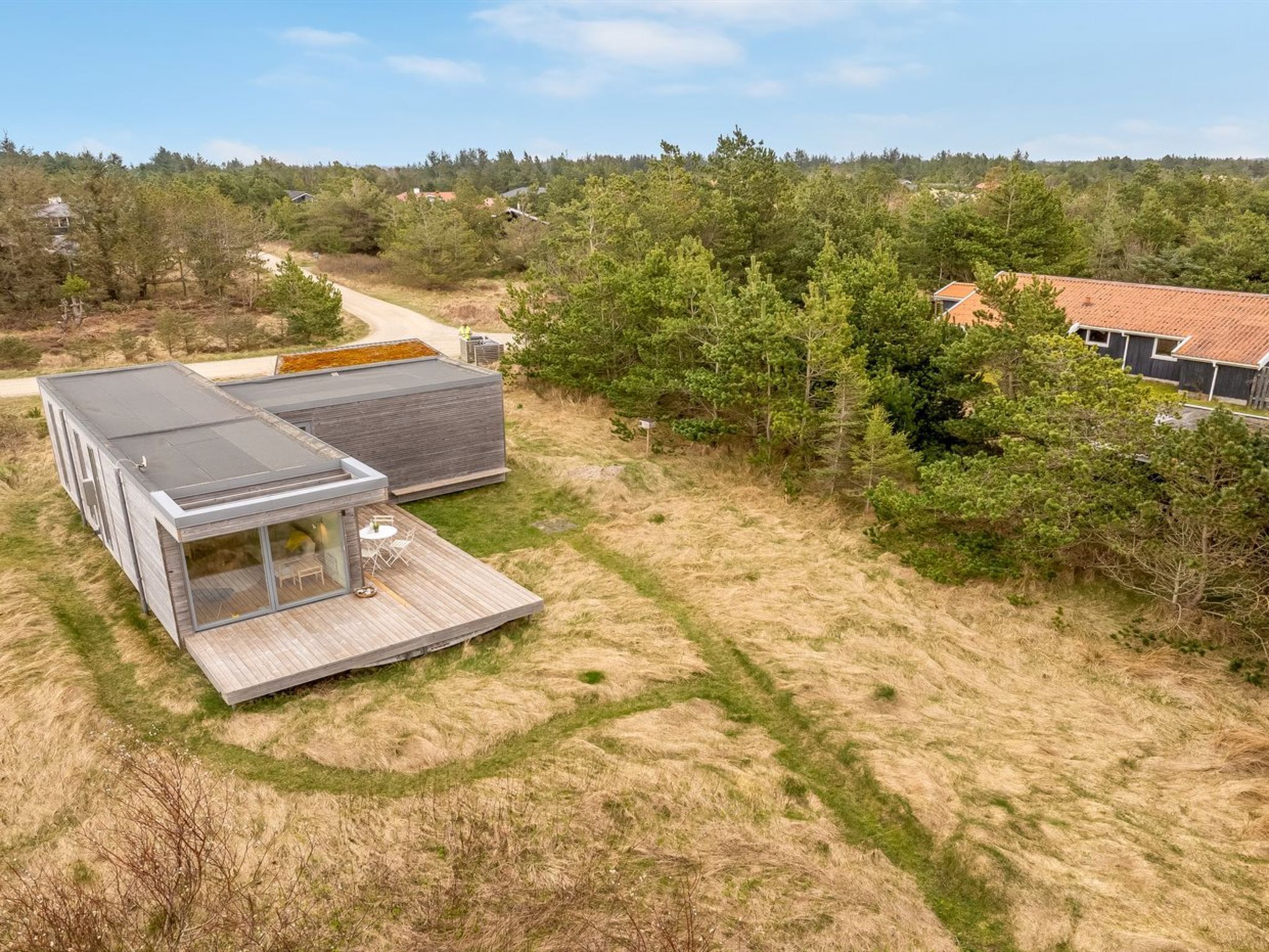 Una casa moderna con una amplia terraza, rodeada de un bosque frondoso y un cielo despejado.