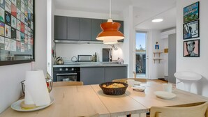 Une cuisine moderne avec un coin repas, comprenant une grande fenêtre, un luminaire suspendu et un mur décoré de tableaux encadrés.