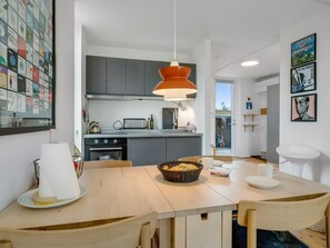 Une cuisine moderne avec un coin repas, comprenant une grande fenêtre, un luminaire suspendu et un mur décoré de tableaux encadrés.