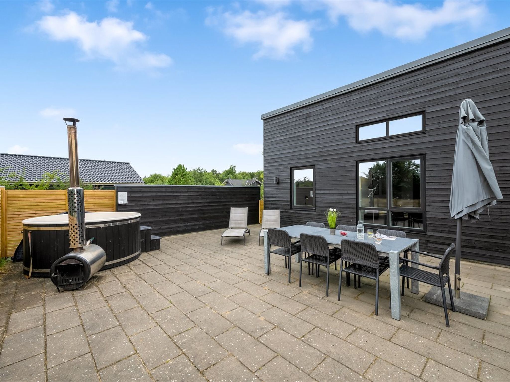 A modern outdoor patio with a hot tub, seating area, and a wooden deck.