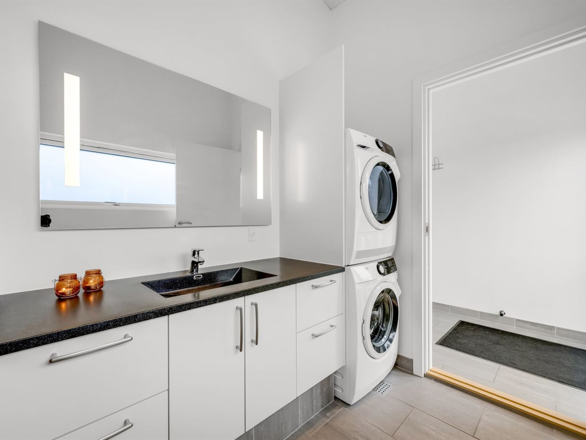 A modern bathroom with a sink, mirror, and stacked washer and dryer.