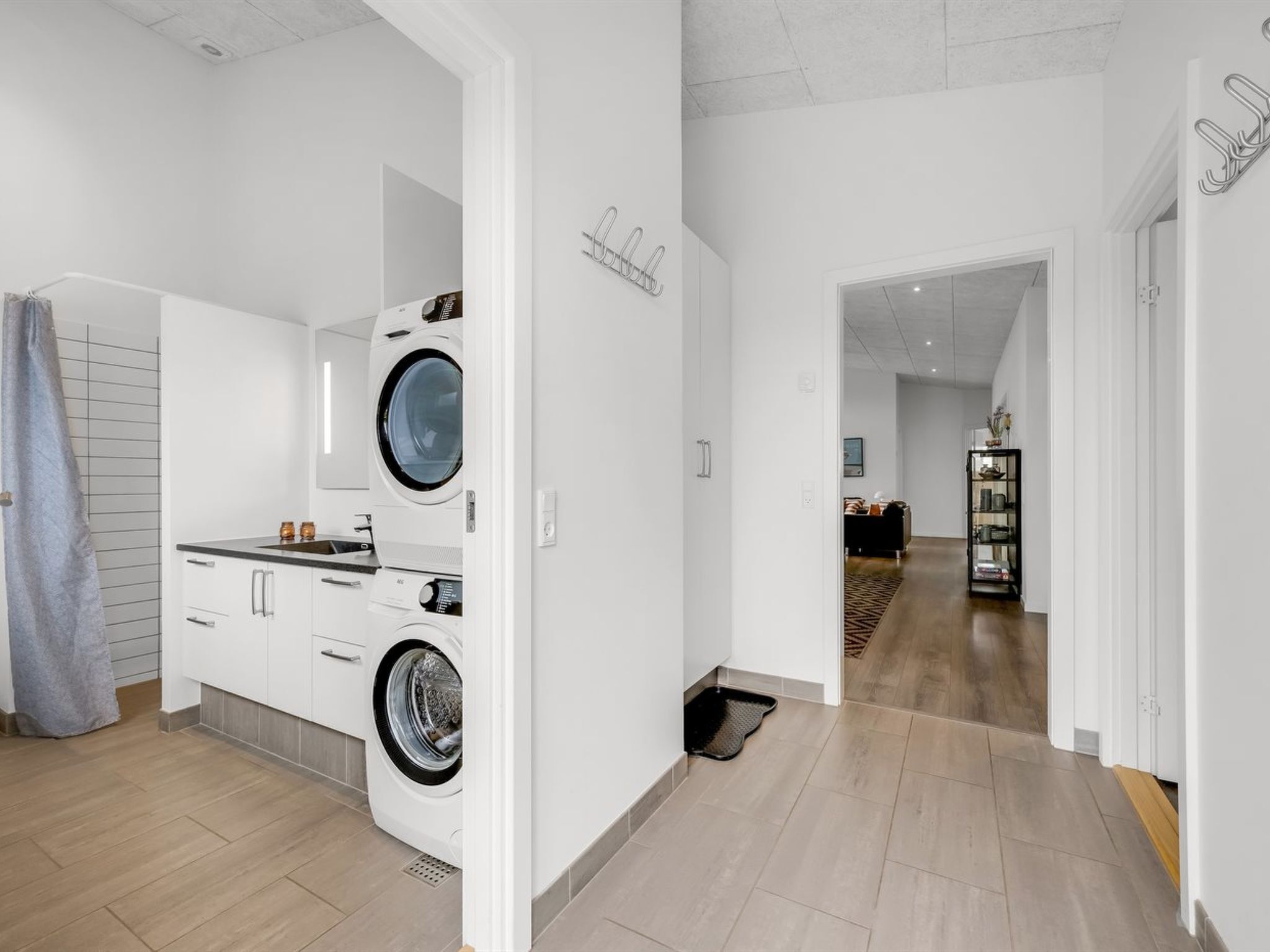 Um apartamento moderno com área de lavanderia, equipado com duas máquinas de lavar de abertura frontal, cozinha com armários brancos e corredor que dá para a sala de estar.