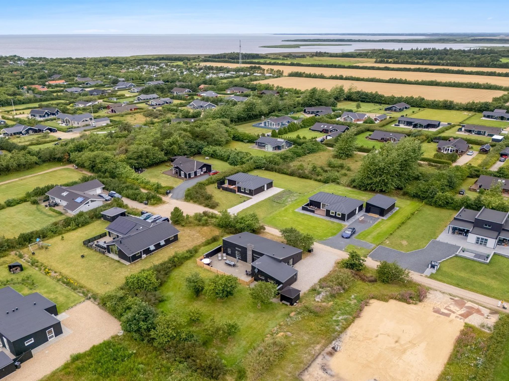 Un quartier résidentiel avec des maisons, de vastes pelouses verdoyantes et une étendue d’eau en arrière-plan.