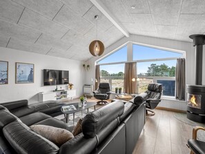 A modern living room with a sectional sofa, a fireplace, and a large window offering a view of the outdoors. - "Alli" - 800m from the sea by Interhome (Fanø)