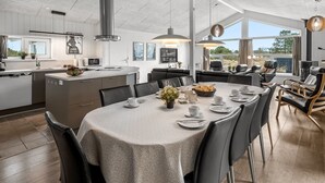 A modern kitchen with a central island, dining area with a table set for six, and a view of the outdoors through large windows.