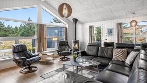 A modern living room with leather furniture, a fireplace, and large windows offering a view of the outdoors.