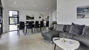 Una sala de estar moderna con un sofá seccional gris, una mesa de centro blanca y un comedor con un ventanal grande.