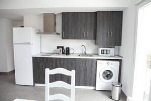 A modern kitchen with grey cabinets, a white refrigerator, a microwave, a coffee maker, and a washing machine. - El chorrillo 4 (Almayate)