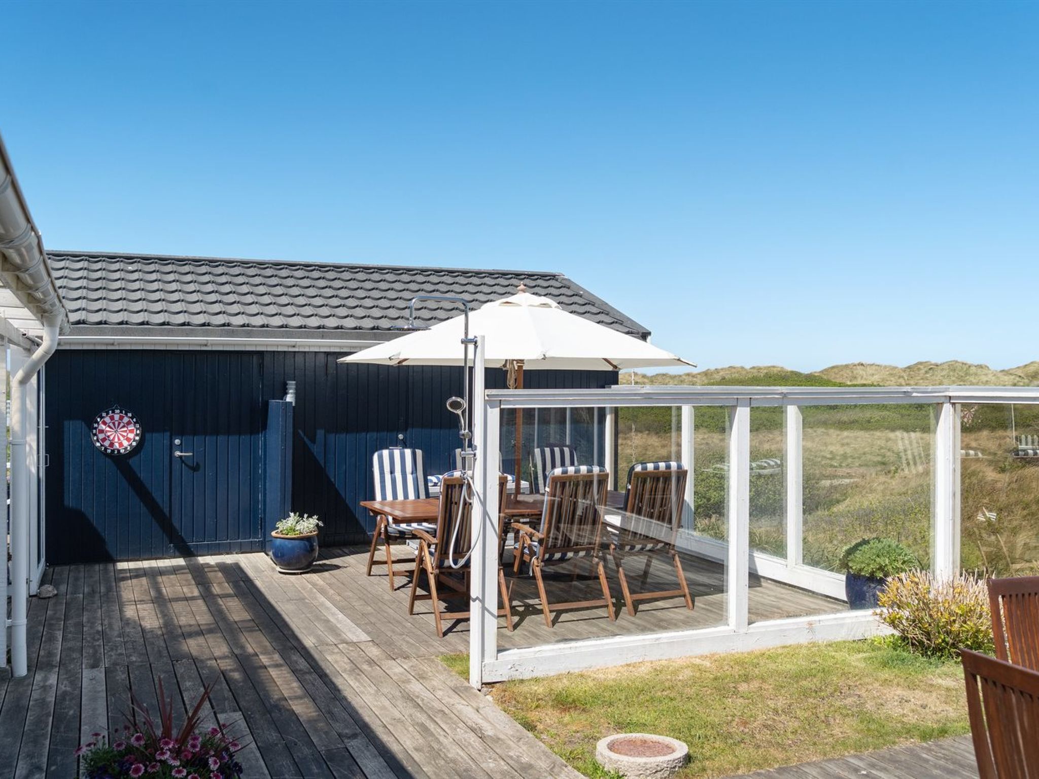 Une terrasse couverte, aménagée avec des meubles en bois et dotée d’un jeu de fléchettes.