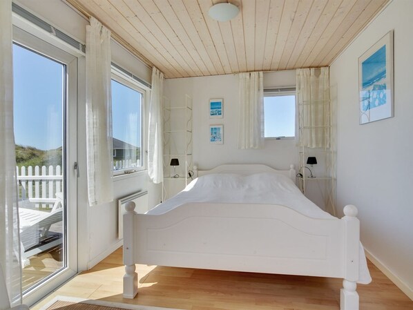 A bedroom with a bed, two windows, a ceiling fan, and a view of the outside.