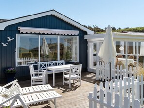 A wooden deck with white furniture, a white picket fence, and a building with large windows and a blue exterior.