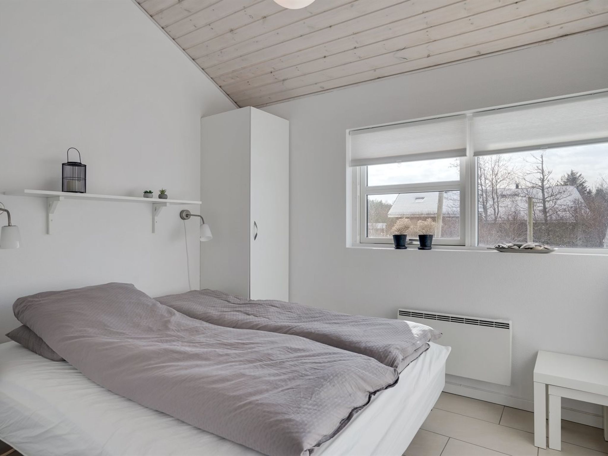 Een slaapkamer met een bed, een raam, een radiator en een kleine tafel.
