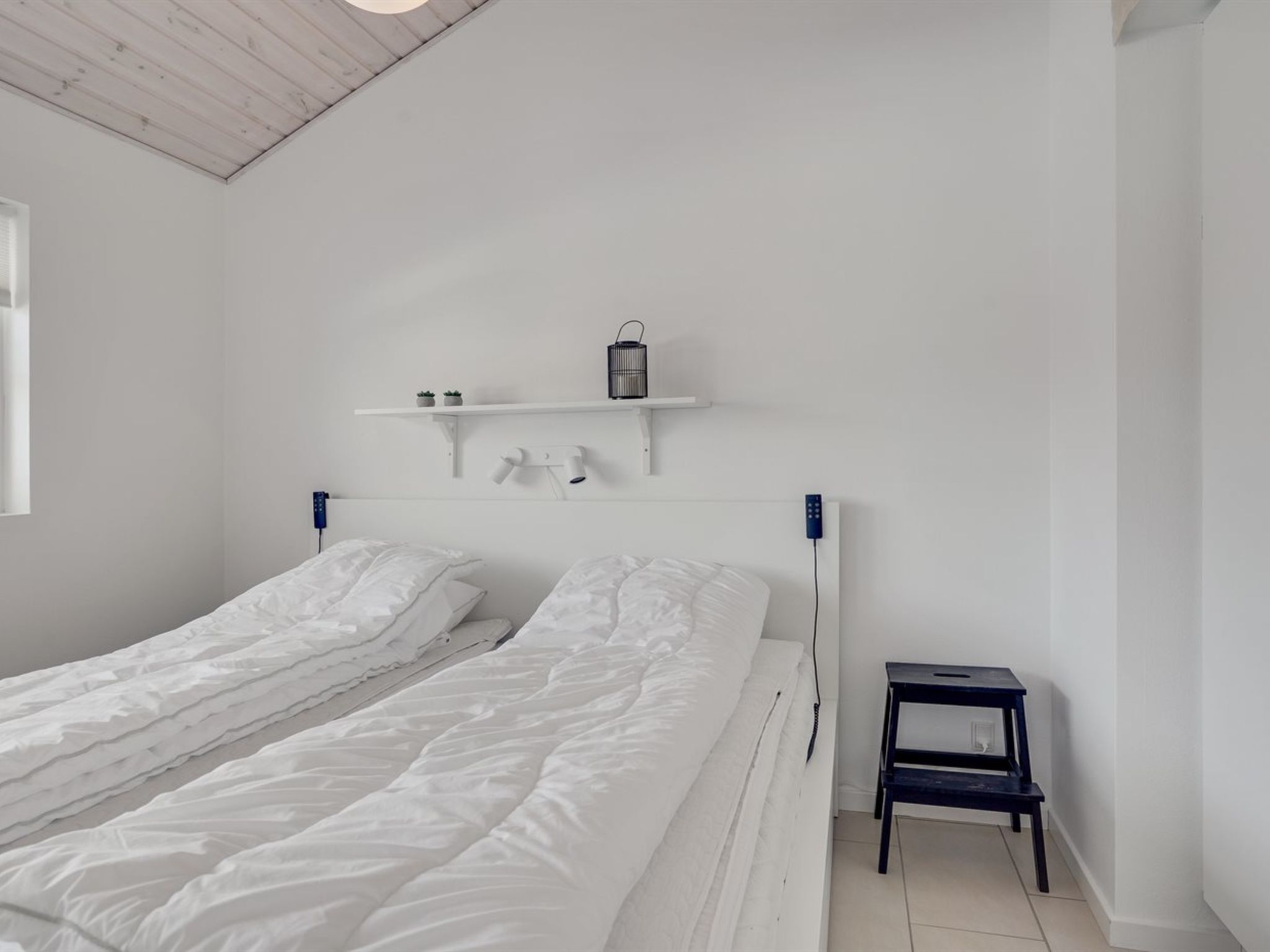 A minimalist room with two single beds, a small nightstand, and a shelf with a lantern.