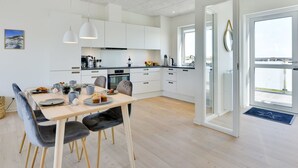 Een moderne keuken met witte kastjes, een eettafel met stoelen en uitzicht door de glazen deur.