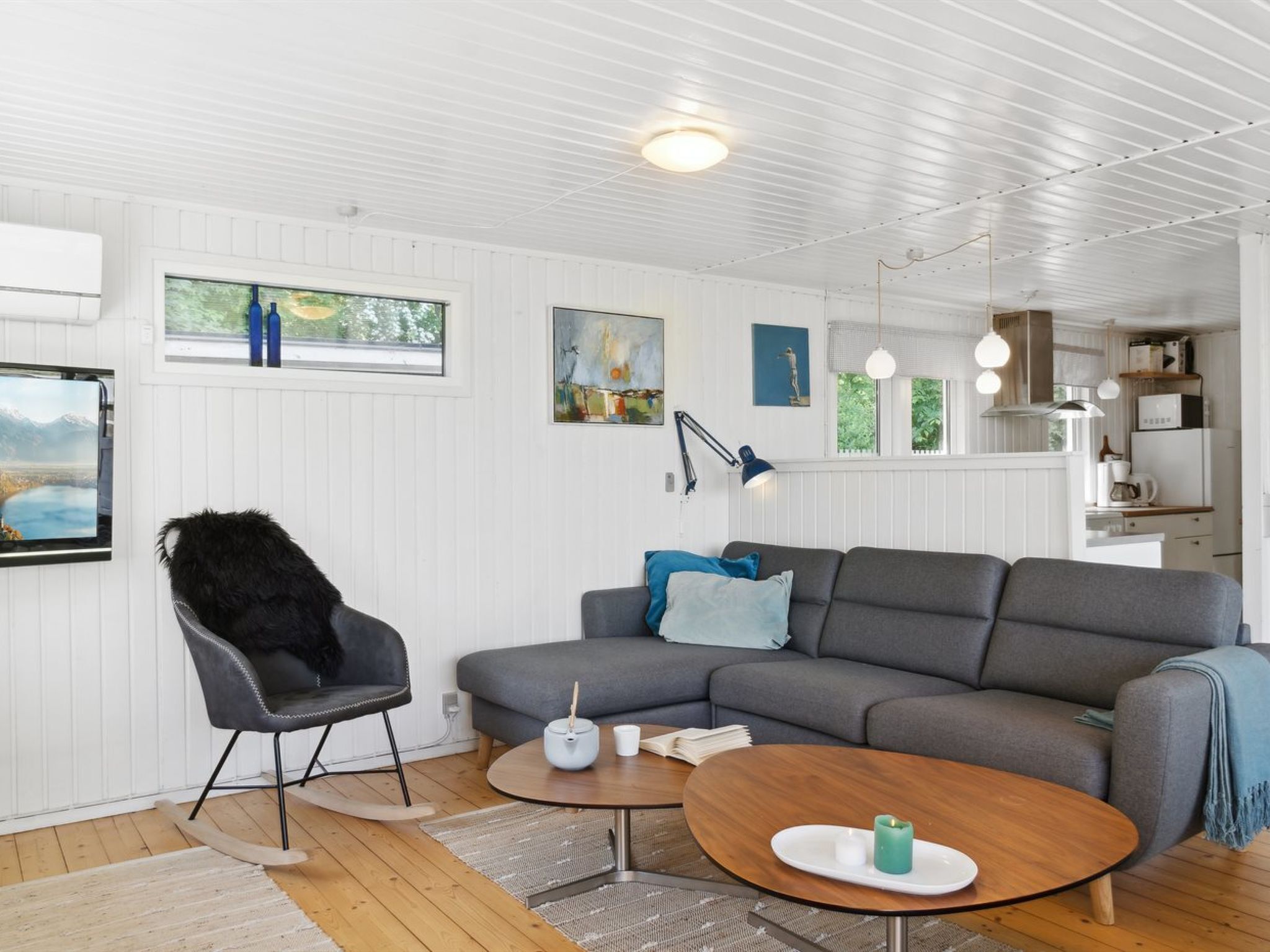 Ein modernes Wohnzimmer mit einem grauen Sofa, einem schwarzen Sessel und zwei runden Holztischen.