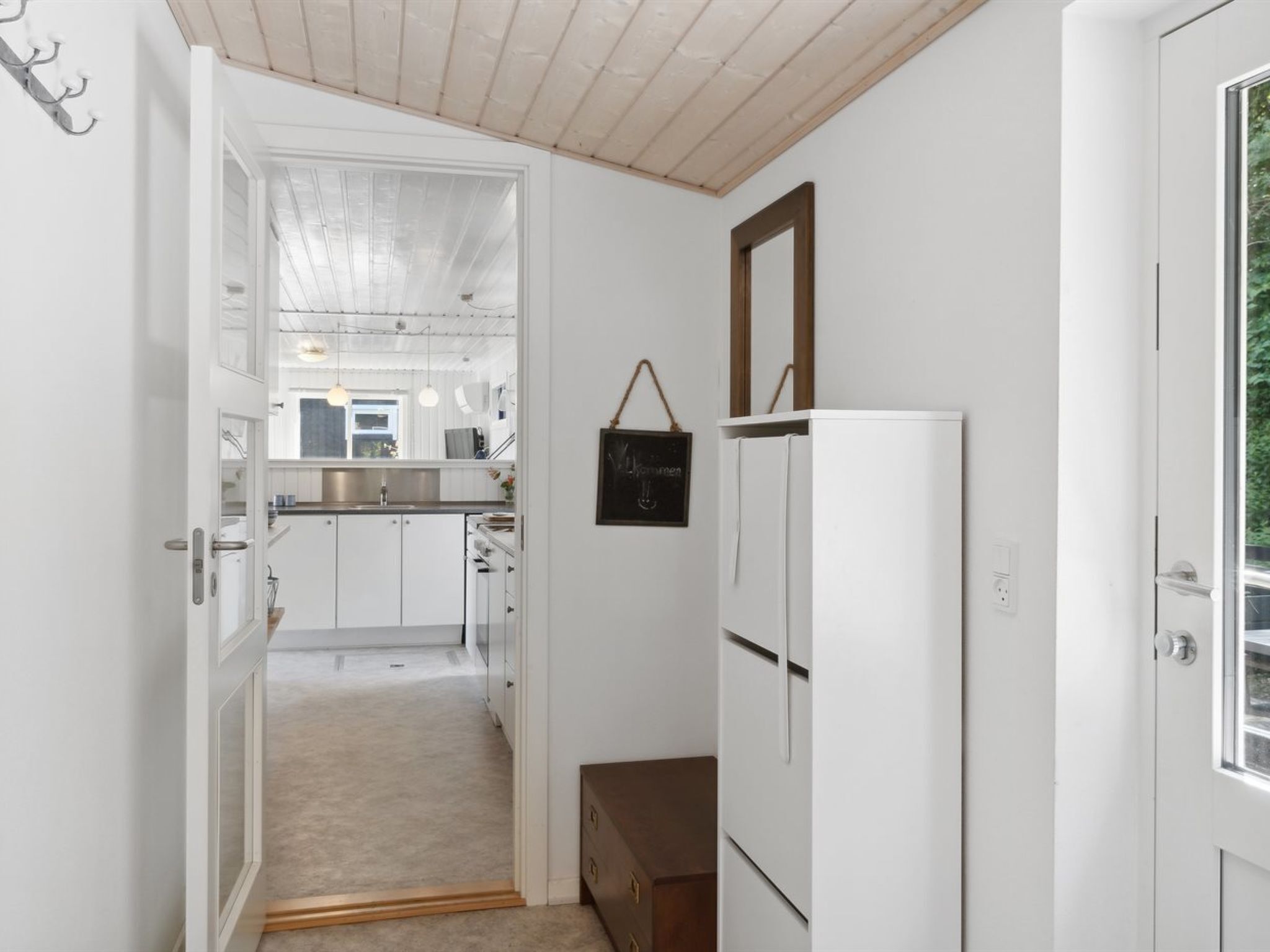 A narrow hallway leading to a kitchen with white cabinets, a refrigerator, and a hanging sign.