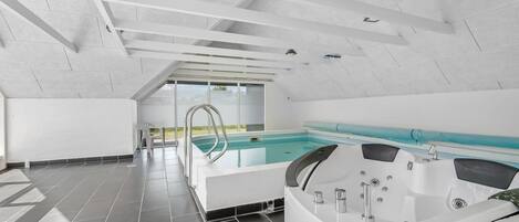 Een modern binnenzwembad met vrij uitzicht op het buitenland, een jacuzzi en een ruim opgezette ruimte.