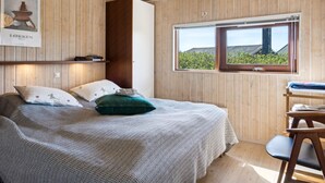 Ein Schlafzimmer mit Bett, Kissen, einer Hängelampe, einem Fenster mit Aussicht und einer Holzwand.