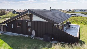 Ein modernes Haus mit Satteldach, einer Terrasse und einem großen Fenster.