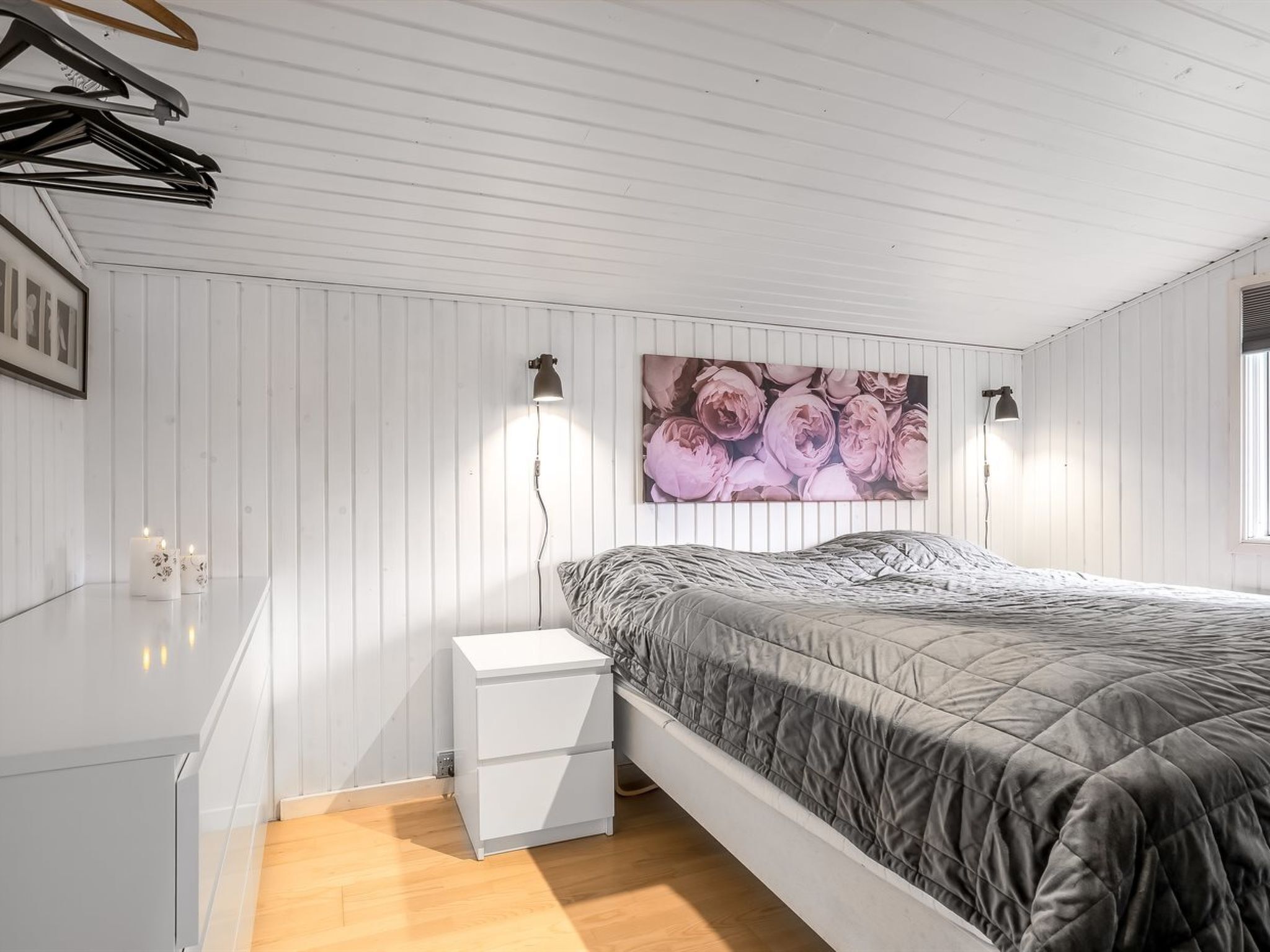 Ein Schlafzimmer mit einem Bett, Nachttischen, einer Wandlampe und einem gerahmten Bild.