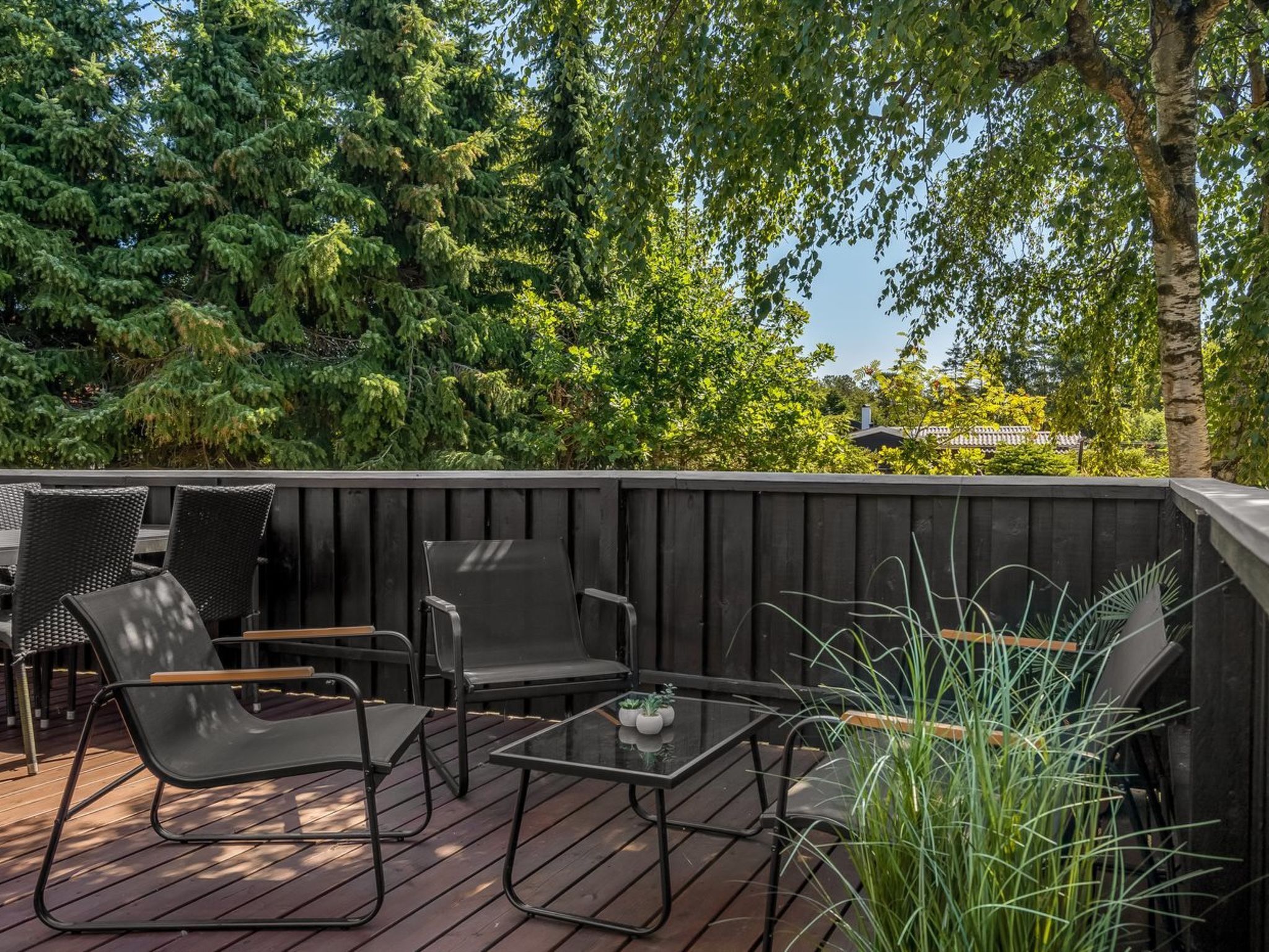 Un espace extérieur aménagé avec des chaises et une table, entouré d’une terrasse en bois et d’une végétation luxuriante.
