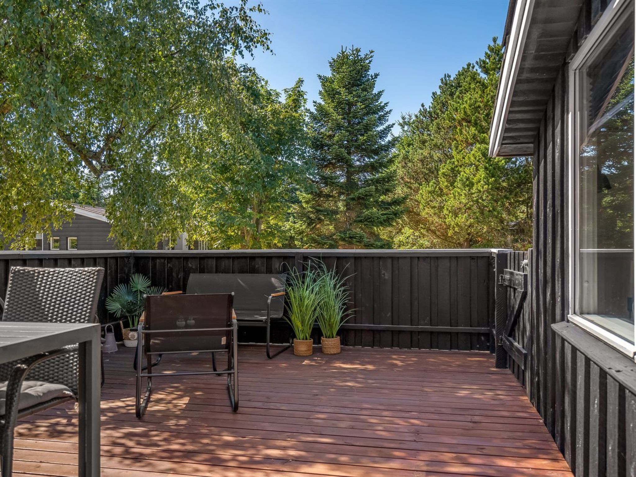 A wooden deck with a grill, chairs, and potted plants.