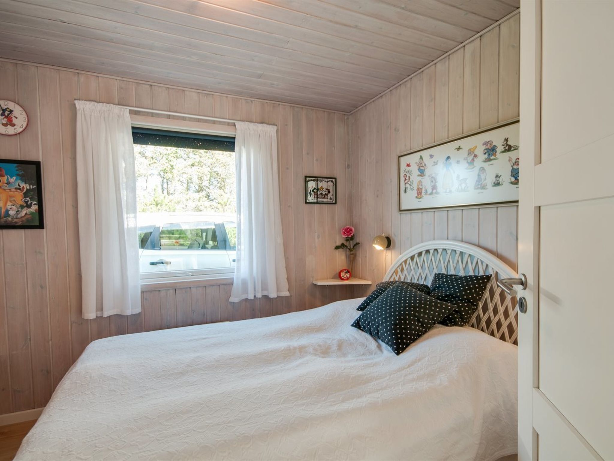 A bedroom with a bed, a window with curtains, a clock, and wall decorations.