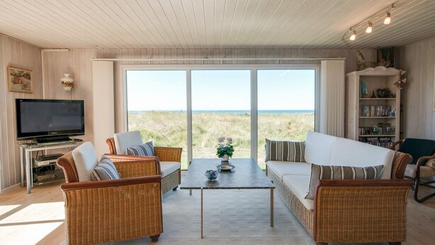 A spacious living room with wicker furniture, a flat-screen TV, and a large window offering a view of the beach. - "Diuri" - 400m from the sea by Interhome (Saltum)