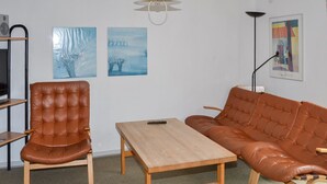 Une pièce comprenant un fauteuil en cuir marron, un canapé en cuir marron et une table en bois. On y trouve deux tableaux accrochés au mur et un lampadaire.