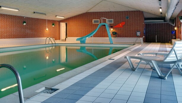 Une piscine intérieure avec un toboggan bleu, un sol carrelé et des chaises longues.