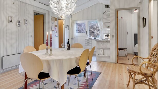 Un espace repas comprenant une table ronde, des chaises, un lustre et une vue sur la cuisine et l’extérieur.