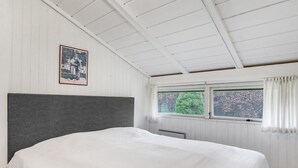 Une chambre avec un grand lit, des murs blancs, un plafond en bois et une fenêtre avec des rideaux.
