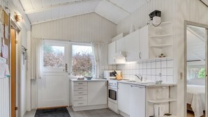 Une cuisine compacte avec des meubles blancs, un four encastré et une fenêtre avec des rideaux.