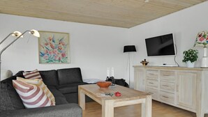 Un salon avec un canapé gris, une table basse en bois, un téléviseur posé sur un meuble et un tableau accroché au mur.