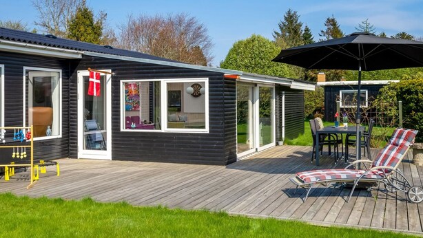Une maison moderne dotée d’une terrasse, d’un coin repas avec mobilier d’extérieur et d’un petit abri de jardin.
