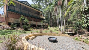 A building with a covered outdoor area, surrounded by a landscaped garden with a fire pit.