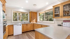Une cuisine moderne avec des meubles en bois, un lave-vaisselle et de grandes fenêtres donnant sur un paysage verdoyant.