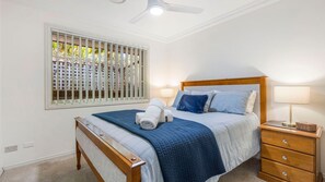 A bedroom with a bed, bedside table, lamp, and a window with blinds.